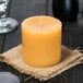 A Sterno beeswax pillar candle burning on a table with a glass of wine in a farm-to-table restaurant.