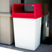 A white Rubbermaid trash can with a red lid.