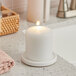 A white Hollowick wax pillar candle sitting on a counter.