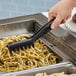 A Cambro black angled plastic spaghetti tong lifting spaghetti from a pan.