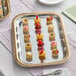 A rectangular metal catering tray with gold trim, displayed with assorted bite-sized desserts.