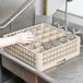 A hand placing a glass in a Vollrath beige glass rack on a counter.