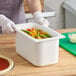 A person in gloves holding a white Carlisle Coldmaster container of food.