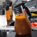 A Tablecraft Tritan dispenser bottle with black lid on a black tray.