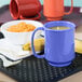 A table with a blue GET Peacock Blue Tritan&#8482; mug filled with food and a spoon.