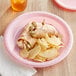 A Classic Pink plastic plate with a sandwich and chips on it.