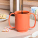 A GET Rio Orange Tritan plastic mug with two handles on a table.