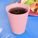 A pink Creative Converting plastic cup with liquid in it on a table next to a plate of food.