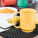 A yellow Tritan mug filled with porridge and a banana on a table.