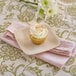 A cupcake with white frosting and coconut shavings on a Bambu square bamboo appetizer plate with a white napkin and a wine glass.