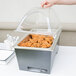 A person holding a clear lid over a container of food in a Sterno silver vein chafing dish.