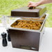 A person using a Sterno Copper Vein chafing dish to serve food on a table outdoors.