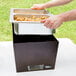 A person putting food into a Sterno copper vein chafer on a table outdoors.