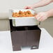 A hand using a Sterno Copper Vein Fold Away Chafer to hold a tray of food.