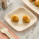A Bambu Veneerware square appetizer plate with food on a table.