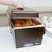 A person holding a Sterno chafer full of food on a table outdoors.