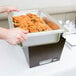 A person holding a tray of food in a Sterno Copper Vein chafer on a table.