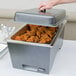A person using a Sterno silver vein chafer to serve food on a white table.