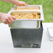 A person holding a Sterno stackable chafer with food in metal pans.