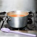 A purple Mercer Culinary high temperature mixing spoon in a pot of soup on a stove.