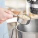 A person using a Tablecraft stainless steel measuring cup to pour oats into a bowl.