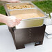 A person putting food into a Sterno Copper Vein chafer container.