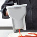 A person using a Vollrath white sauce dispenser to pour orange sauce onto pizza dough.