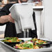 A man using a Vollrath sauce dispenser to pour white liquid onto a salad.