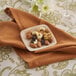 A Bambu Veneerware disposable bamboo tasting plate with nuts, raisins, and a wine glass on a table.