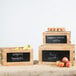 A Tablecraft 3-piece wooden crate riser set with black chalkboards holding apples on a table.