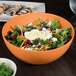 A close up of a salad in an orange round bamboo bowl.