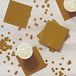 A group of cups of liquid and gold foil Creative Converting beverage napkins on a table.