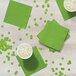 A table set with Fresh Lime Green Creative Converting beverage napkins and cups of liquid.
