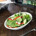 A Libbey Infinity oval porcelain bowl filled with salad and vegetables on a table.