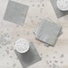 A stack of shimmering silver Creative Converting beverage napkins on a table with cups of water.