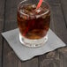 A glass with ice and a straw with a Creative Converting Shimmering Silver beverage napkin on the table.