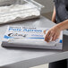 A person putting a box of polypropylene aprons on a counter.