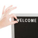 A hand touching a black felt sign with white letters on a stand.