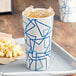 A white paper cup with a blue and white cylindrical container with blue lines filled with ice tea and popcorn.