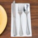 A white napkin with silverware on a yellow plate.