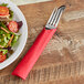 A fork and knife wrapped in a Classic Red napkin next to a plate of salad.