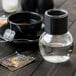 A Libbey glass jar with clear liquid next to a cup of tea with a tea bag tag.