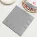 A Creative Converting Shimmering Silver paper dinner napkin on a table next to a white cake.
