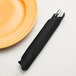 A fork in a black velvet paper dinner napkin next to a plate.