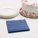 A white cake with red sprinkles next to a navy blue Creative Converting beverage napkin on a table.