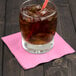 A glass with ice and a straw on a pink napkin.