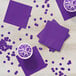 A group of amethyst Creative Converting beverage napkins on a table with cups of purple liquid.