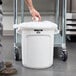 A man putting a plastic bag in a white Rubbermaid BRUTE trash can.