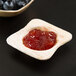 A wooden bowl with a wooden spoon with red jelly in it on a table.