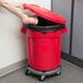 A person putting a coffee cup in a red Rubbermaid BRUTE trash can.